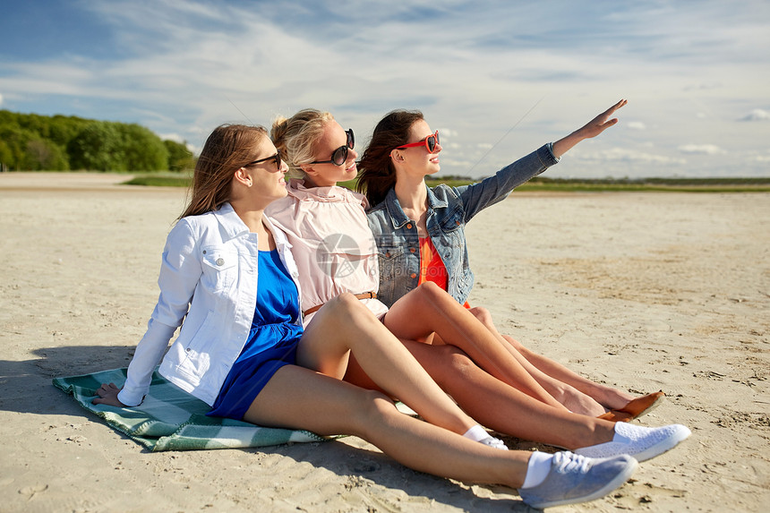 暑假,假期,旅行人们的群微笑的轻女戴着太阳镜,坐沙滩毯子上,指着什么东西图片