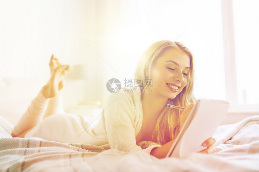 休息,睡觉,舒适人的快乐的轻女人床上写笔笔记本家里的卧室图片