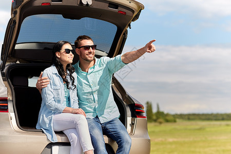 旅行,暑假,公路旅行,休闲人们的幸福的夫妇拥抱打开的掀背车后备箱,并指向户外图片