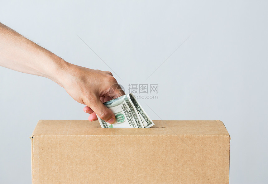 慈善财政资金投资人的男手把美元钱放进捐赠箱图片