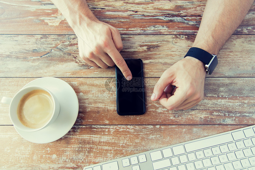 商业,技术人的近距离的男手着智能手机,戴着手表与咖啡键盘木桌上图片