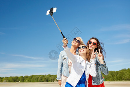 暑假,假期,旅行,技术人的群微笑的轻女海滩上自拍杆上用智能手机拍照图片