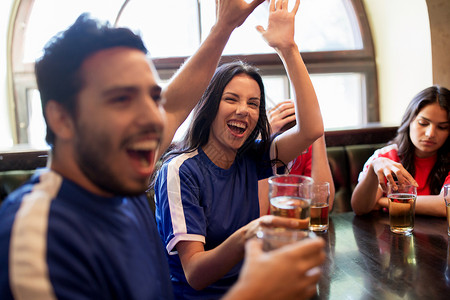 体育娱乐活动快乐的球迷朋友喝啤酒,击掌庆祝胜利酒吧酒吧,支持两支同衬衫颜色的球队背景图片