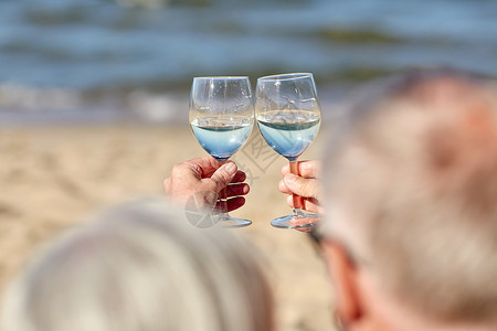 龄璃杯家庭龄假期休闲人的夏日海滩上,幸福的老夫妇碰杯背景