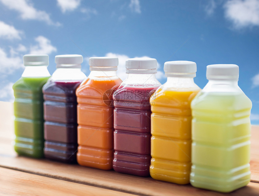 健康饮食,饮料,饮食包装塑料瓶与同的水果蔬菜汁木制桌子上的蓝天背景图片