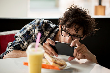 休闲,食物,饮食人的男人与智能手机拍摄他的午餐咖啡馆图片