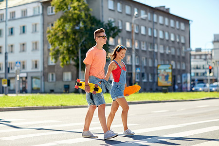 暑假,极限运动人们的快乐的青少夫妇与短现代巡洋舰滑板穿越城市人行横道图片