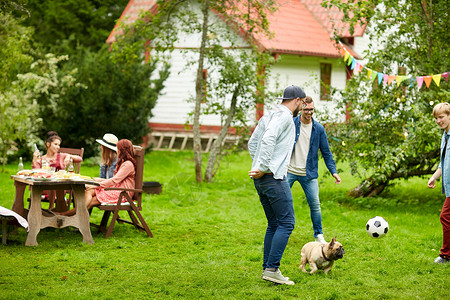 休闲,假期,人宠物的快乐的朋友夏天的花园聚会上狗踢足球图片