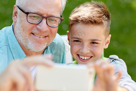 家庭,世代,技术人的快乐的祖父孙子与智能手机自拍夏季公园图片
