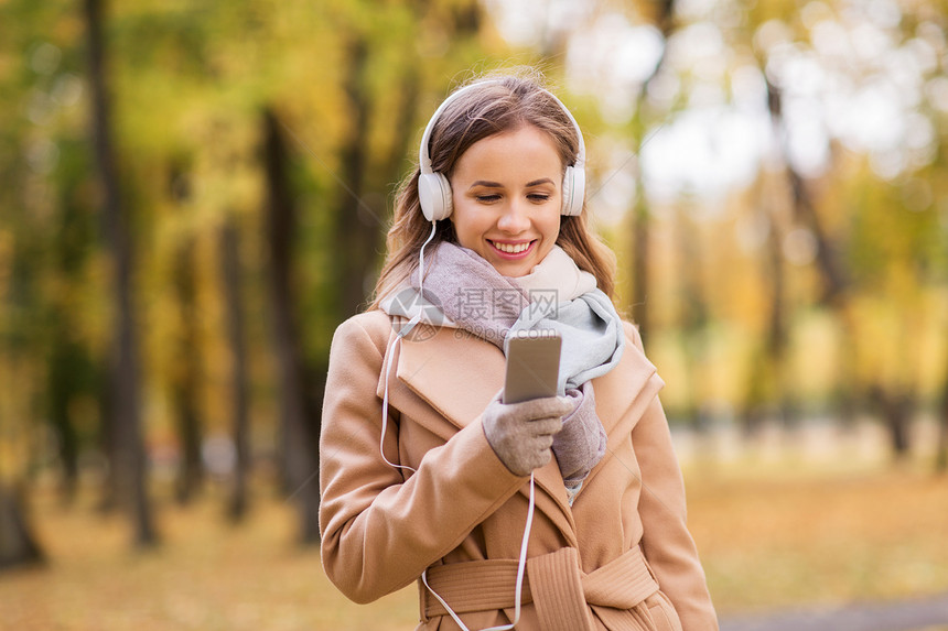季节,技术人的美丽的快乐轻女子戴着耳机,智能手机上听音乐,秋天的公园散步图片