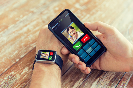商业,技术人的近距离的男手持智能手机佩戴智能手表与来电接口屏幕上图片
