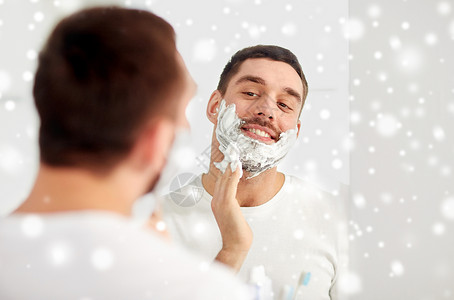 美容,卫生,剃须,美容人的微笑的轻人看着镜子,用剃须泡沫家里的浴室雪图片