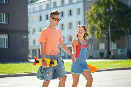 暑假,极限运动人们的快乐的青少夫妇与短现代巡洋舰滑板穿越城市人行横道图片