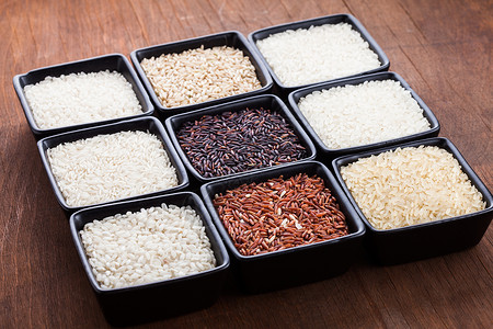木制桌子上黑色碗里的各种米饭各种类型的大米高清图片