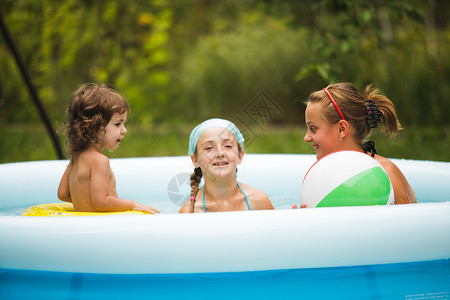 令人放松的浮动三个女孩蓝色的游泳池里游泳,玩球游泳池里的女孩背景