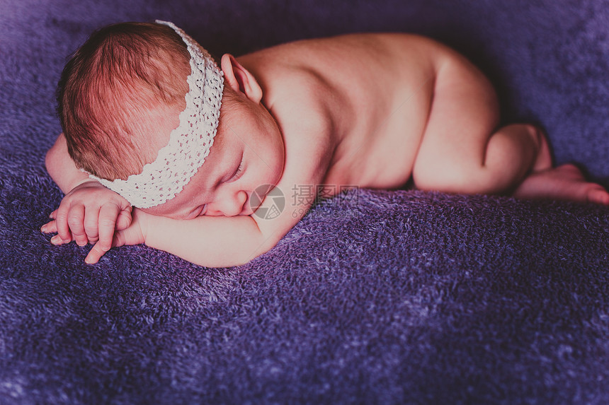 熟睡的婴儿,头上白色花边,躺紫色毯子上的肚子上迷人的熟睡婴儿的肖像图片