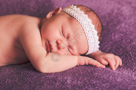 熟睡的婴儿,头上白色花边,躺紫色毯子上的肚子上迷人的熟睡婴儿的肖像图片
