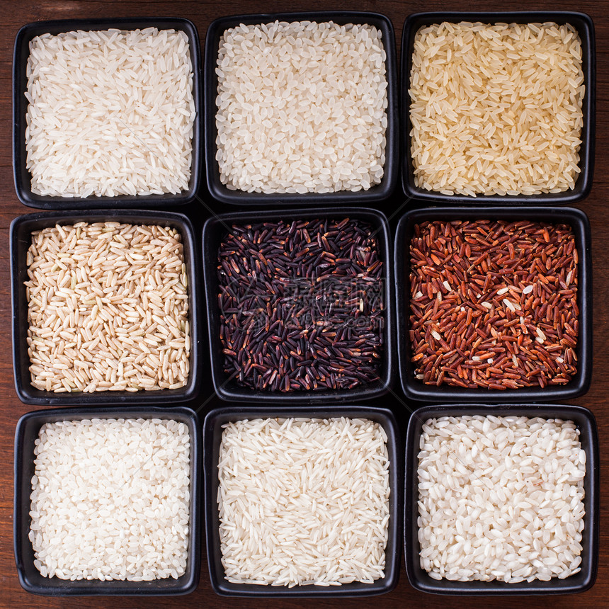 木制桌子上黑色碗里的各种米饭各种类型的大米图片