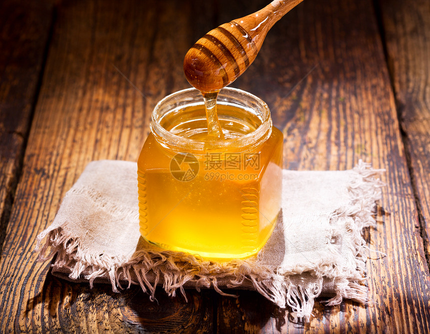 把蜂蜜倒进木桌上的罐子里图片