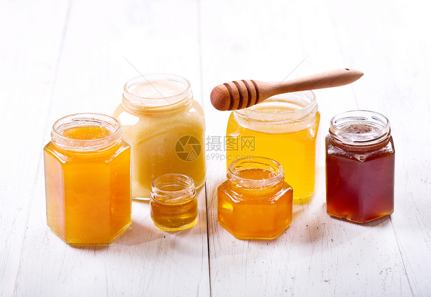 木制桌子上璃瓶中的各种蜂蜜图片