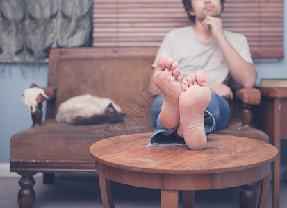 个赤脚的轻人正家里的沙发上休息,旁边只猫睡觉图片