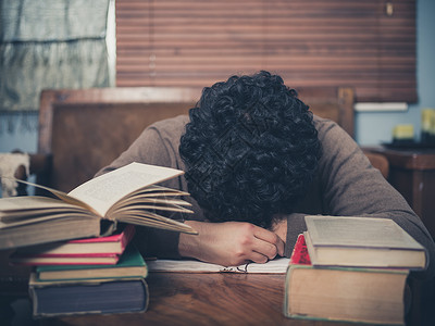 个疲惫的学生被书包围的咖啡桌上睡着了图片