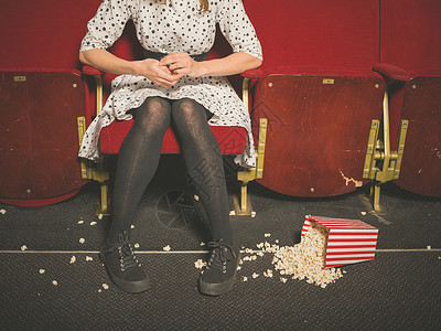 个轻的女人坐电影院里,桶爆米花洒她前的地板上图片