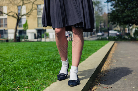 个穿着裙子的轻女人正绿草地旁的公园里散步图片