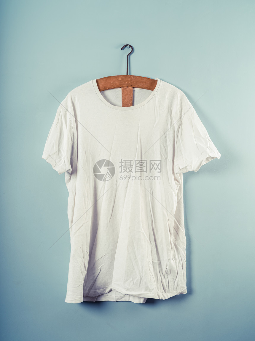 件白色的t恤挂个木制衣架上,靠蓝色的墙上图片