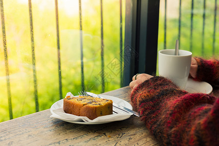 个轻女人的手靠窗的桌子上休息,因为她正喝茶吃蛋糕图片