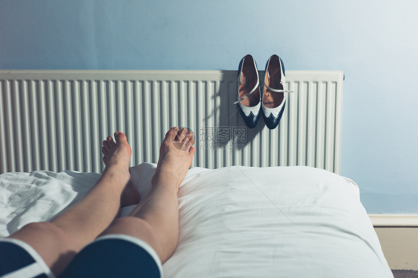 个轻的女人穿着高跟鞋走了整天后,躺床上休息图片