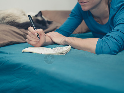 个轻的女人只猫躺床上,用钢笔记事本笔记图片