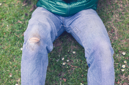 个穿着牛仔裤膝盖破洞的时髦轻人坐草地上背景图片