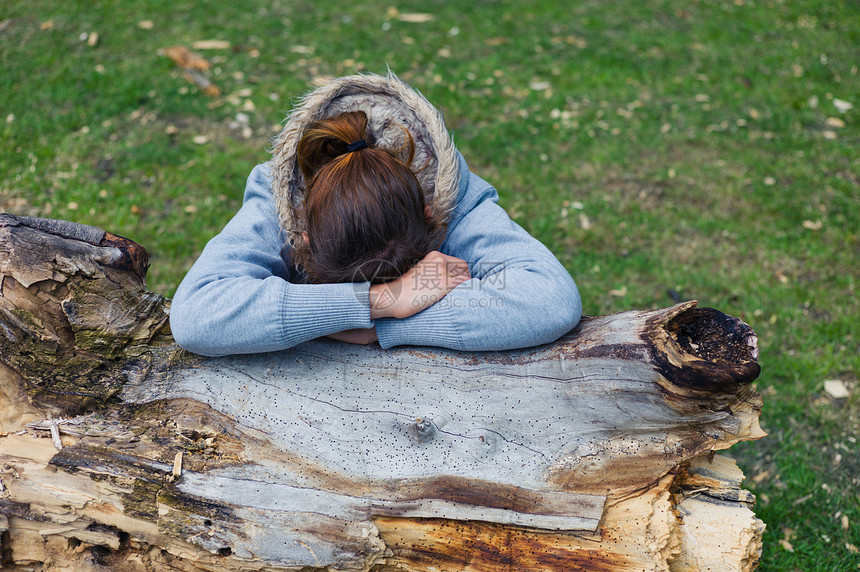个悲伤的轻女人正公园里的树干上休息图片