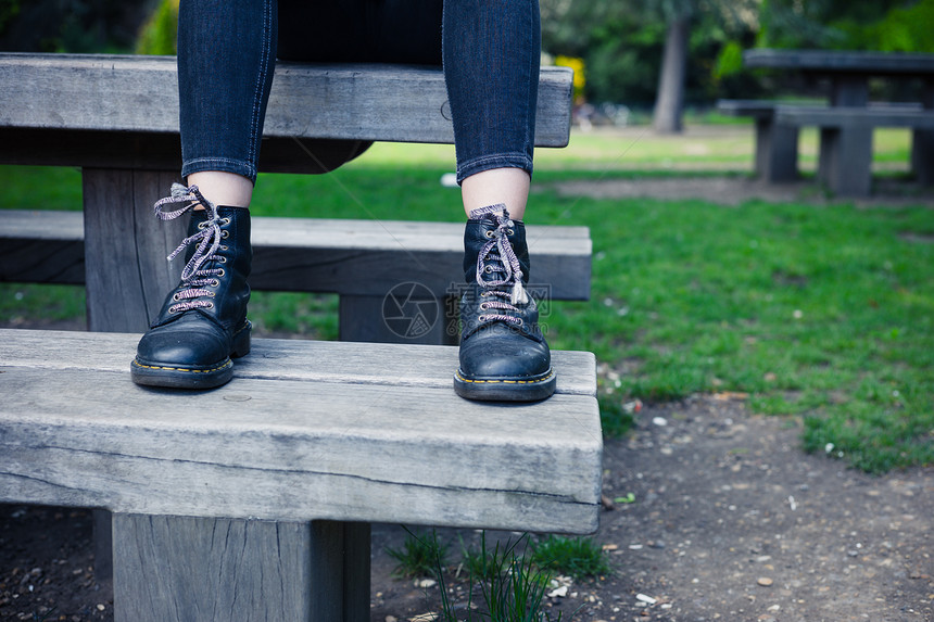 个穿着靴子的轻女人坐公园的长凳上图片