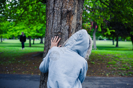 个戴帽衫的可疑人物躲公园的棵树后高清图片