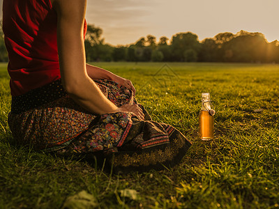个轻的女人日落时公园里喝饮料放松图片