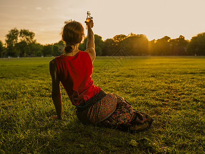 个轻的女人正公园里喝酒,正举她的瓶子向夕阳致敬图片