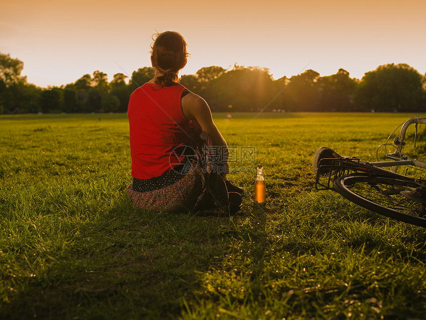 个轻的女人公园里欣赏日落,旁边个瓶子辆自行车图片