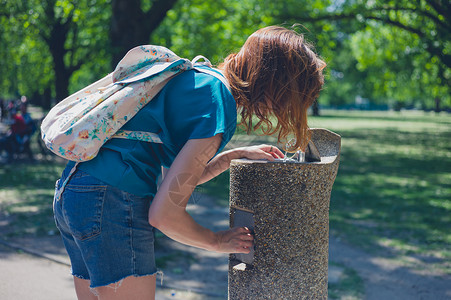 个轻的女人正夏天个阳光明媚的日子里公园里的喷泉里喝水图片