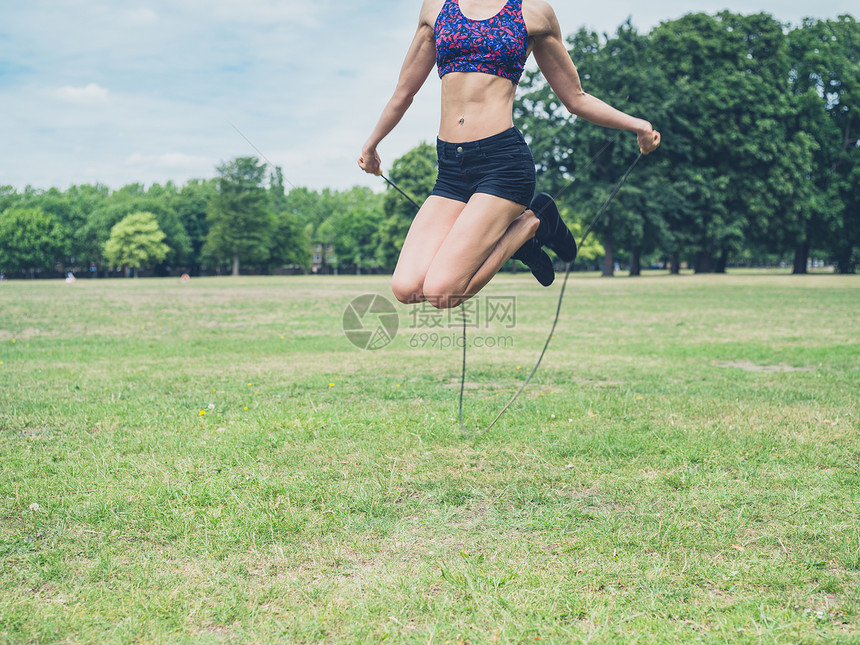 个健康运动的轻女子夏天的公园里跳绳图片
