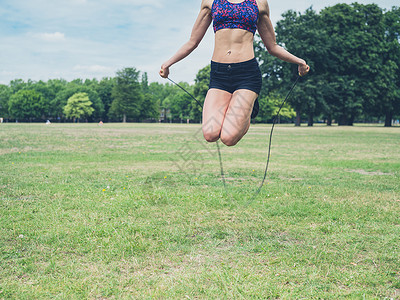 个健康运动的轻女子夏天的公园里跳绳图片