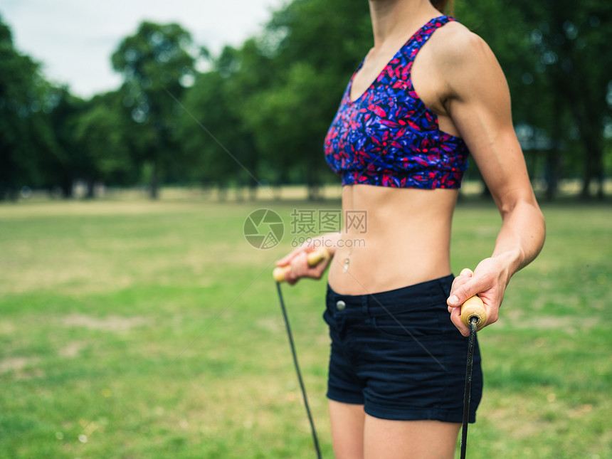 个健康而运动的轻女人站公园里的草地上,着根跳绳图片