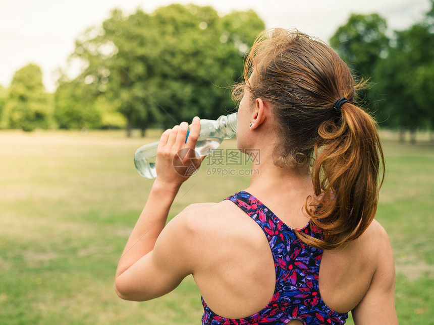 个运动的轻女人正公园里用瓶子喝水图片