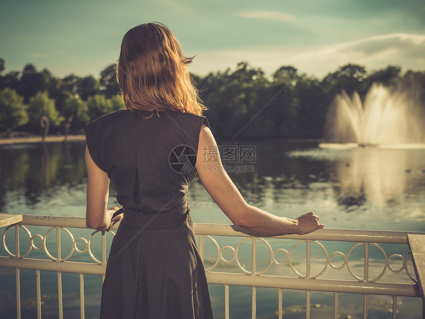 位优雅的轻女子日落时站公园里的湖边的老式过滤镜头图片
