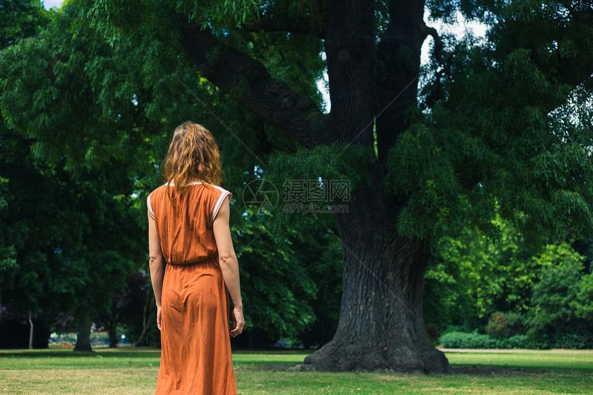 个轻的女人正公园里散步,站棵大树旁边图片
