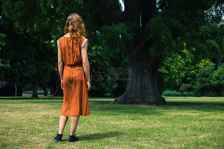 个轻的女人正公园里散步,站棵大树旁边图片