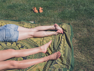 两个轻女人的腿,因为他们阳光明媚的天外的草地上放松图片