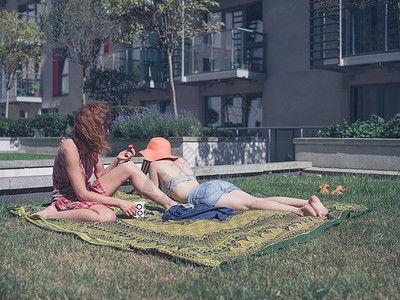 个阳光明媚的日子里,两个轻的女人正城市地区外的草地上放松图片