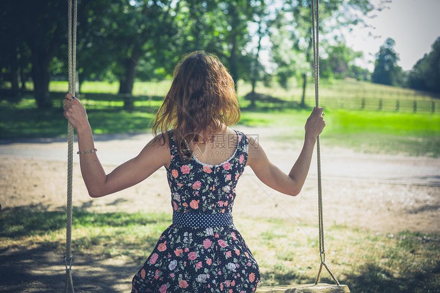 个穿着连衣裙的轻女人夏天坐外的秋千上图片